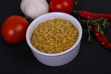 Raw bulgur in the bowl with tomatoes and garlic
