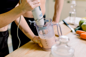 Obraz na płótnie Canvas Healthy eating, fitness lifestyle, proper nutrition. Close-up photo of pretty sport woman and man making healthy smoothie. Woman is using hand blender