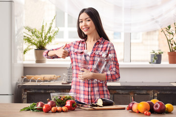 Young girl at kitchen healthy lifestyle standing with water bottles looking camera cheerful showing thumb up