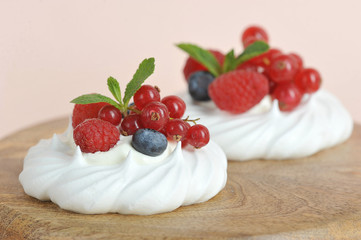 Meringues with fresh berries of raspberry, blueberry and red currant. The dessert is decorated with mint leaves. Light background. Close-up.