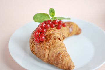 Croissant with red currants on a white plate. Light beige background. Close-up. Macro shooting.