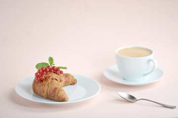 Croissant with red currant berries and a cup of coffee on a light background. The concept of a delicious breakfast. Free space waiting for text placement. Close-up.