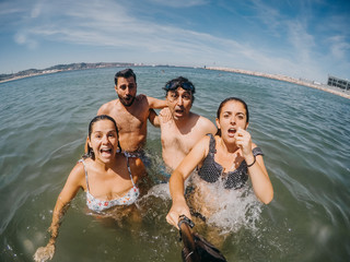 Obraz premium .Funny group of friends taking pictures together and playing in the water on the beach. Enjoying a summer day in north of Spain. Lifestyle