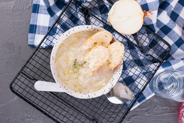 Onion soup with cheese and croutons in a white cup on a gray stone background. Traditional french soup in light colors. Country food. Free space for text.