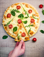 close up of male hand taking slice of pizza with tomatoes and herbs over wooden table