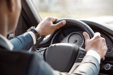 Young businessman driver wearing watch sitting inside car holding steering wheel driving close-up back view