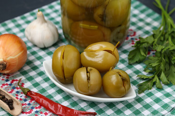 Marinated stuffed green tomatoes in a plate and in a jar on the table