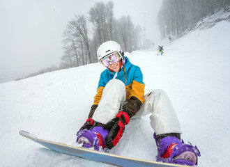 Portrait of positive woman snowboarder, fastened to snowboard on background of falling snow with poor visibility weather in high mountains of Caucasus at Krasnaya Polyana