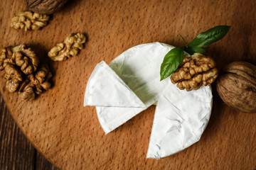 Camembert or Brie cheese with walnut kernels on wooden wooden background. Copy space. white mold grows on top Penicillium camemberti. 