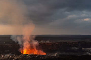 A volcanic crater at dawn. The glow and smoke from the lava is visible. It is the Kilauea volcano on Hawaii's big island.