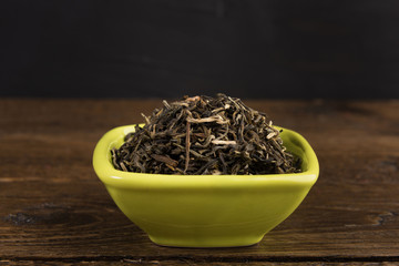 Fototapeta premium dry green tea in a clay bowl isolated on wooden table on black background