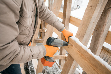 Carpenter using electric screwdriver. Man builds a roof of wooden planks. Attic renovation. Building construction outdoor. Countryside house. Farm householding. - 251891780
