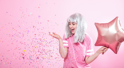 Funny Girl with silver hair gives a smile and emotion on pink background. Young woman or teen girl with balloons and confetti