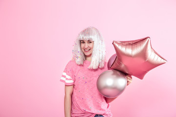 Funny Girl with silver hair gives a smile and emotion on pink background. Young woman or teen girl with balloons and confetti