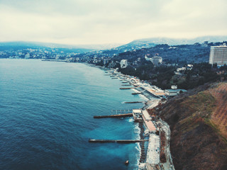 Obraz premium Aerial panorama of winter Yalta in cloudy day, embankment with breakwaters, old European city on Black Sea, town on mountains, beautiful resort landscape