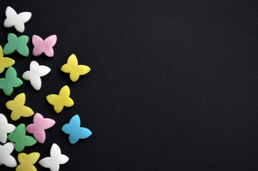 Sugar multicolored butterflies on left side on black background, the concept of spring and March 8, with copyspace