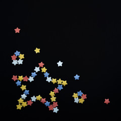 Star folded from multicolored sugar pastry stars on a black background with copyspace on square shape
