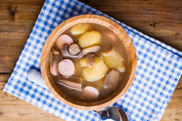soup with sausages and potatoes on a wooden background in a bowl. Traditional German rustic soup. Rustic style photo. Free space for text.
