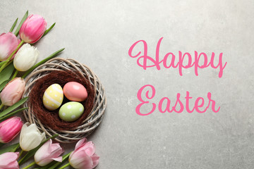 Flat lay composition with painted eggs in wicker nest and text Happy Easter on color background