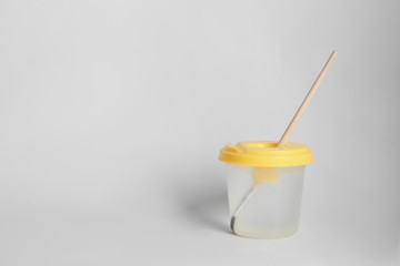 Paint brush in cup of water on light background. Space for text