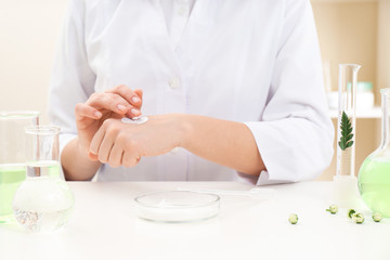 Female dermatologist testing skin care product at table, closeup