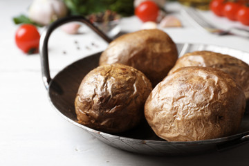 Frying pan with tasty baked jacket potatoes on wooden table, closeup