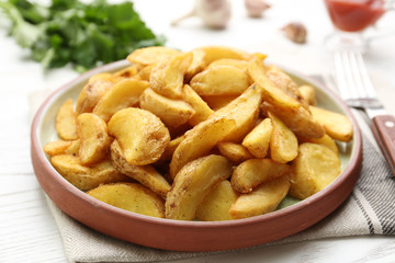 Plate with tasty baked potato wedges on wooden table