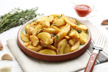Plate with tasty baked potato wedges on wooden table