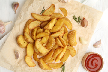 Delicious baked potato wedges on wooden background, top view