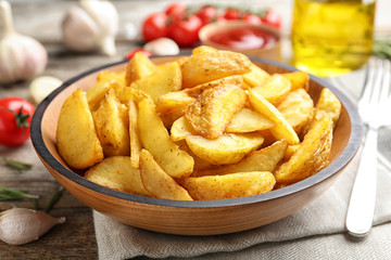 Plate with tasty baked potato wedges on wooden table