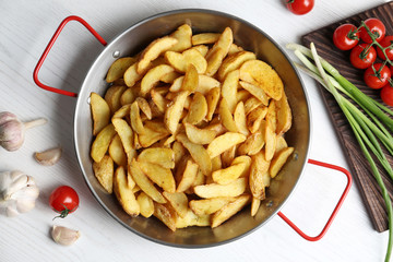 Frying pan with tasty baked potato wedges on wooden background, top view