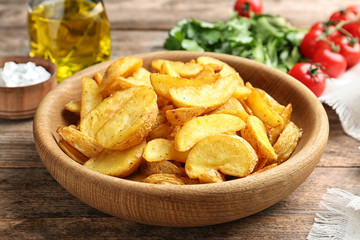 Bowl with tasty baked potato wedges on wooden table