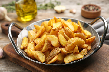 Frying pan with tasty baked potato wedges on wooden table