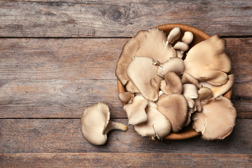 Fototapeta premium Bowl of delicious organic oyster mushrooms on wooden background, top view with space for text