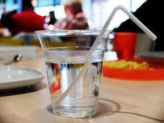 Plastic glass with water and a straw on the table in the cafe