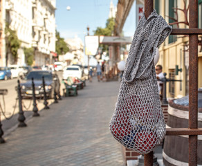Gray string bag with red knitting yarn hanging on an old rusty metal fence