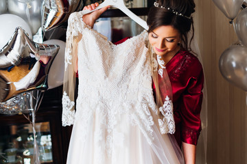 Pretty brunette bride holding delicate white wedding dress on a