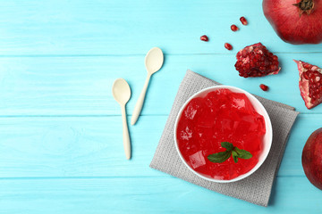 Flat lay composition with red jelly in bowl and pomegranate on wooden background. Space for text