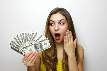 Portrait of a shocked pretty girl looking at bunch of money banknotes isolated over white background