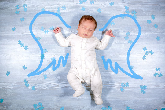 Cute little sleeping baby flying with angel wings over wooden background. Newborn baby with painted angel wings