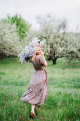 girl blonde in a dress goes with a bouquet of lilac on a background of green garden