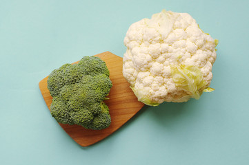 Top view of broccoli and cauliflower on the wooden cutting board. The blue background. Healthy food