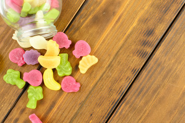 Obraz na płótnie Canvas Colored gummy fruit candy spilled, on a brown wooden table