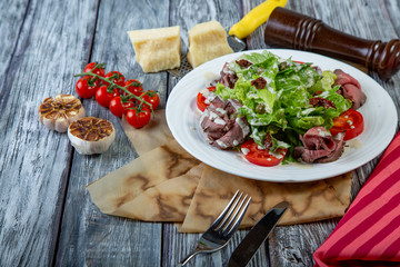 Salad leaves with sliced roast beef and sun-dried cherry tomatoes on wooden background