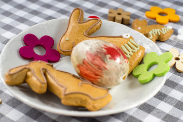 Group of gingerbread animals and symbols on white plate on checkered tablecloth, two bunnies in love, Easter egg hunt