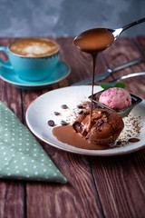 Chocolate lava cake Molten with ice cream on plate and cappuccino. Balls of ice cream in cup . Dark black background.