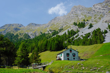 Fototapeta na wymiar Rural house built in Italian mountain architecture style under the mountain peak surrounded by green meadows