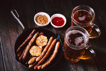 beer and snacks. bar table. restaurant, pub, oktoberfest food. two mugs of craft lager and frying pan with delicious homemade grilled sausages. friday party atmosphere, craft brewery concept