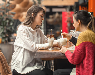 Two happy women are sitting in a cafe, drinking milkshakes,