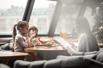 Happy young women mother with children sitting at dinner table and talking in restaurant